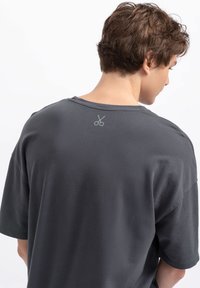 Grijze korte mouw t-shirt van zacht materiaal, met een subtiele schaarlogo op de bovenrug gedrukt. Relaxte pasvorm met een ronde hals.