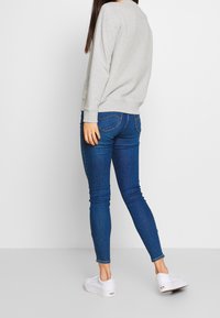 Felpa grigia, jeans skinny blu, sneakers bianche. Tessuto morbido, polsi e orlo a coste, texture in denim, silhouette aderente, design minimale.