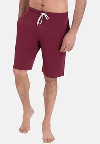 Shorts bordeaux en tissu doux, avec une ceinture élastique et un cordon blanc, arrivant au milieu de la cuisse sur un modèle pieds nus.