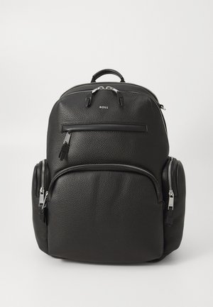 Sac à dos en cuir noir avec une finition texturée, poches zippées à l'avant, et une poignée supérieure ; présente un logo et des accents en métal argenté.
