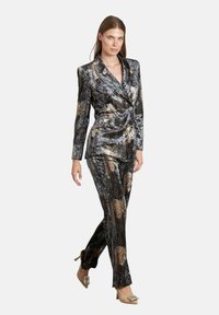 Completo brillantinato nero e oro con giacca aderente, bottoni doppi, e pantaloni dritti; abbinato a tacchi decorati.