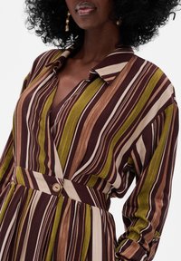 Sukienka koszulowa w paski, w której dominują odcienie brązu, zieleni i beżu, z długimi rękawami i zaznaczoną talią. Gładka faktura materiału.