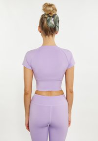 Top sportiv scurt de culoare lila cu mâneci scurte, textură netedă și design ajustat. Asortat cu colanți lila cu talie înaltă.
