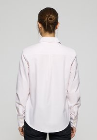 Camicia a maniche lunghe in rosa chiaro con righe verticali bianche, dotata di colletto a pieghe e polsini con bottoni, realizzata in un tessuto liscio.