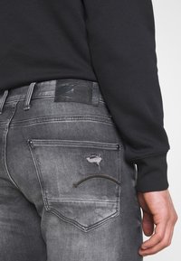 Grijze denim jeans met een versleten achterzakontwerp en zwart leren label. Heeft een slim fit en een vervaagde textuur, met contrasterende stiksels.