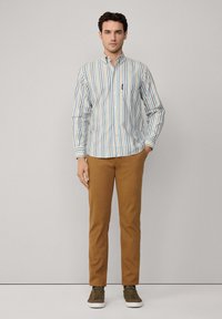 Camisa de botones a rayas en colores azul, blanco y marrón, combinada con pantalones marrones y zapatillas verde oliva. Tejido suave, corte entallado.