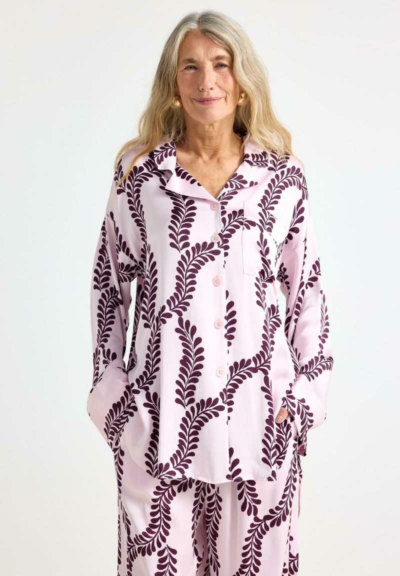 Lyserød pyjamas sæt med mønster og bladdesign i mørk lilla, med lange ærmer, krave og lomme detaljer.