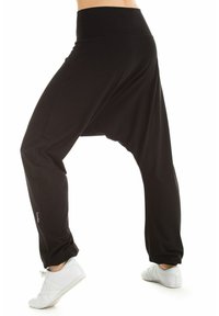 Zwarte, losse harem broek met een brede tailleband en taps toelopende benen, gemaakt van zachte stof. Voorzien van een subtiele logodetail aan de zijkant.