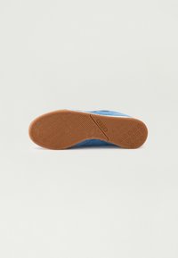 Chaussure de sport en suede bleu avec une semelle en caoutchouc gomme, présentant des motifs de semelle circulaires et une finition texturée sur le dessus.
