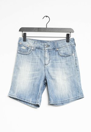 Short en denim bleu clair avec poches avant et passants de ceinture suspendu sur un cintre noir sur fond blanc.