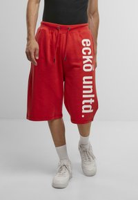 Red sweat shorts made of cotton with side pockets, a drawstring waist, and bold white text reading "ecko unlt." on the left leg.