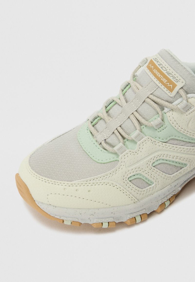 Chaussure de course gris clair avec des accents vert menthe, en maille et en matériau synthétique, tige texturée, col rembourré et semelle extérieure en caoutchouc beige.