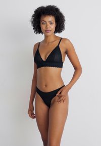 Black lace bralette with triangular cups and scalloped edges, paired with matching black thong. Both feature a soft texture and minimal coverage.