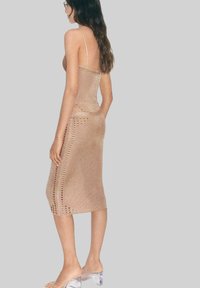 Knit midi dress in a light beige color with adjustable spaghetti straps, featuring a crochet pattern along the sides. Clear heeled sandals.