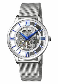 Montre automatique argentée avec un bracelet en mailles. Dispose d'un boîtier transparent révélant les mécanismes internes, des marqueurs d'heure bleus et des chiffres romains.