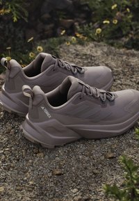 Hellbraune Sportschuhe mit strukturiertem Obermaterial, abgerundetem Zehenbereich und gepolsterter Sohle. Sie verfügen über Schnürsenkel und ein Logo an der Seite.