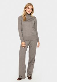 Světle hnědý rolák s žebrovanou texturou, v kombinaci s odpovídajícími širokými kalhotami. Měkký pletený materiál s volným střihem.