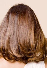 Bruin, middellang haar met subtiele highlights, vertonend zachte golven en een natuurlijke glans tegen een lichtbeige achtergrond.