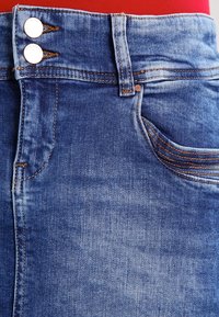 Modrá džínová sukně s vysokým pasem, dvojitým zapínáním na knoflíky, obrysem kapes a kontrastním stehem. Materiál má hladkou strukturu.