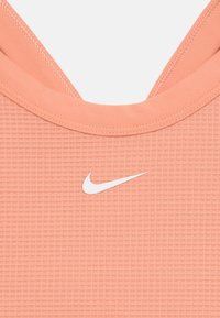 Nike sportinis viršus iš tekstūruoto persikų spalvos audinio su išpjovimu prie kaklo; priekyje yra balta logotipas.