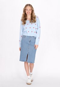 Maglione azzurro chiaro con motivi a forma di cuore rossi, abbinato a una gonna di jeans lunghezza ginocchio con uno spacco frontale. Sneakers bianche con dettagli colorati.