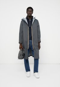 Hallhallane vihmavari, millel on kapuuts, kollased tõmblukuaktsendid ja pikad varrukad. Kantud tumesinise pluusi peal ning koos siniste teksade ja valgete tossudega.