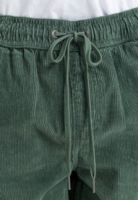 Groene corduroy broek met een trekkoord in de taille. Textuurstof met verticale ribbels en zilverkleurige hardware aan de uiteinden van het trekkoord.