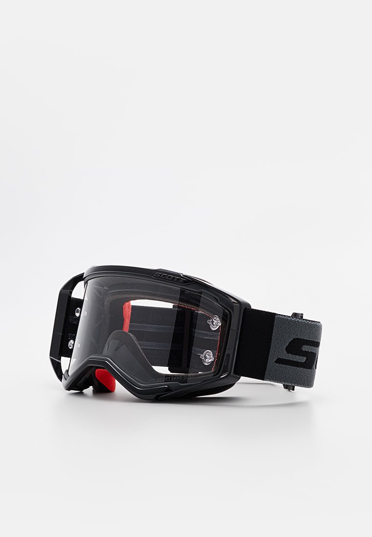 Occhiali da motocross neri con lente trasparente, fascia regolabile rossa e nera e fori di ventilazione sui lati per un migliore flusso d'aria.