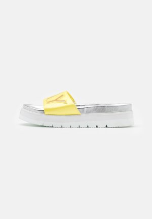 Slide-sandal med en sølvfarvet fodseng, en tyk hvid sål og en bred gul rem broderet med et stort bogstav V.