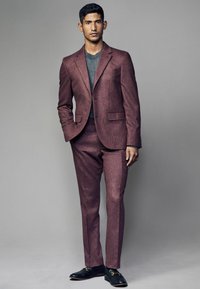 Costume sur mesure bourgogne avec une finition texturée, associé à un t-shirt noir à col rond. Des mocassins noirs avec des accents dorés complètent le look.