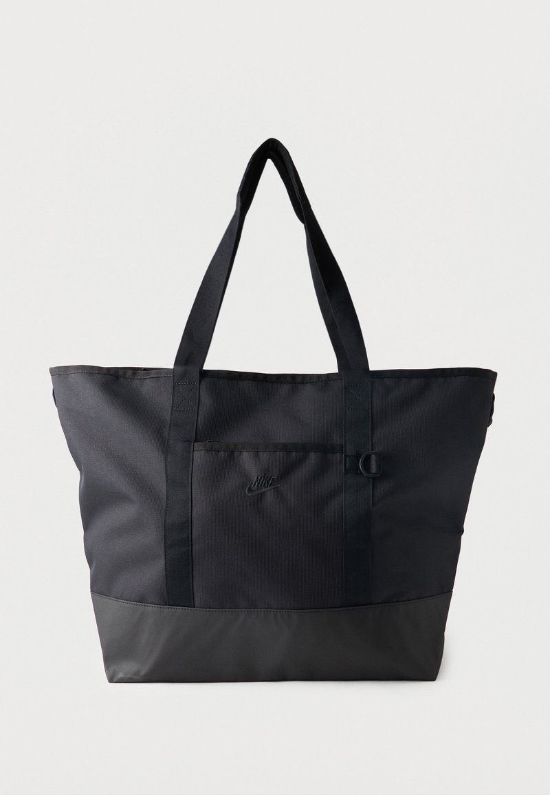 Sac fourre-tout noir Nike avec longues anses, poche avant avec logo et panneau inférieur renforcé, sur fond blanc uni.