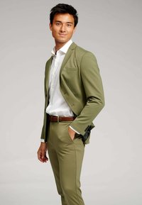 Grøn jakkesæt med en stram pasform, der har en notch lapel, enkelt knap og brystlomme. Sæt det sammen med en hvid skjorte og et brunt bælte.