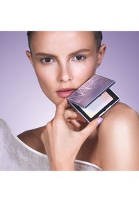 Komakte Make-up-Palette, die von einer Person gehalten wird, mit einem glänzenden, schimmernden Deckel und buntem Puder darin. Sanfte Haut mit natürlichen Tönen.