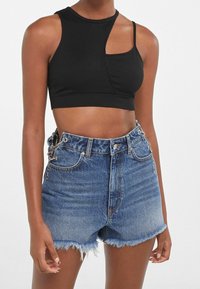 Svart ribbad kort tanktopp med en asymmetrisk utskärning, matchad med högmidjade blå denimshorts med fransiga kanter och kedjeaccenter.