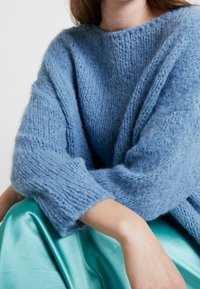 Ljusblå stickad tröja med lös passform, texturerat tyg och vida ärmar, kombinerad med en blank teal satinunderdel.