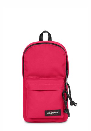 Mochila de nylon roja con forma redondeada, con un bolsillo frontal, acentos negros y un lazo para colgar. Logotipo exhibido en la parte frontal.
