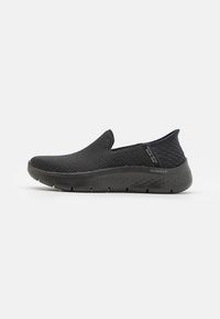Black slip-on shoes with a textured mesh upper and a thick, cushioned sole featuring a diamond pattern for added grip and support.