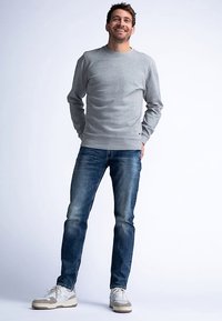 Szara bluza crew-neck z miękkiego materiału, zestawiona z ciemnoniebieskimi dżinsami. Model nosi białe trampki z beżowymi akcentami.