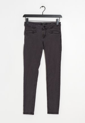 Jean slim noir avec fermeture éclair et bouton à l'avant, deux poches fendues à l'avant, suspendu à un cintre noir sur fond blanc.