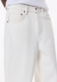 Beli jeans iz bele denima z visokim pasom, klasičnim petim žepnim dizajnom in srebrno obarvanimi dodatki z rahlo teksturo ter ravnim krojem.