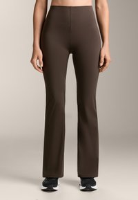Barna sport leggings rugalmas anyagból. Magas der�ék, bővülő fazon, sima textúra, fekete sportcipővel párosítva.