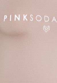 Jasnoróżowy sportowy top o podłużnej fakturze, z białym napisem „PINK SODA” i geometrycznym logo serca poniżej.