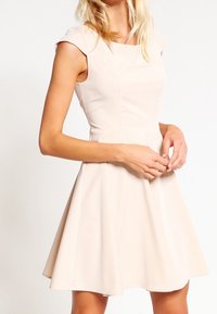Robe A-line beige clair avec de courtes manches courtes, un bustier ajusté et une jupe évasée, fabriquée à partir d'un tissu lisse avec des couture minimales.