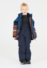 L'ensemble d'hiver pour enfants comprend une veste isolante bleue et marron, un pantalon sombre et des chaussures noires, avec de multiples poches et fermetures éclair.