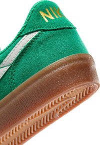 Zöld velúr sneaker fehér részletekkel, texturált gumi talppal és arany "NIKE" felirattal a saroknál. Klasszikus dizájn megerősített varrásokkal.