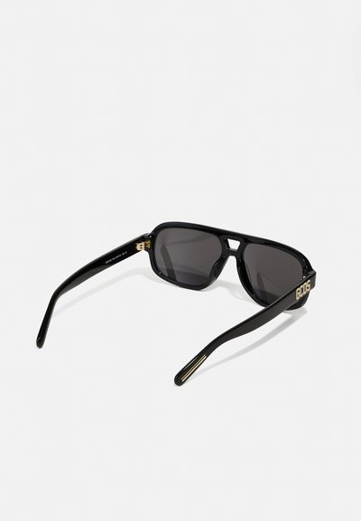 Black sunglasses with a glossy finish, gray lenses, and a geometric frame design. Features gold accents on the temples with the brand logo.