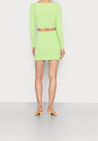 Ljusgrön ribbad tvådelad set som består av en kortärmad topp med lång ärm och en minikjol med en scalloped fåll, matchad med gula klacksandaler.