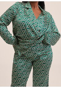 Costume en satin vert avec un motif de chaînes complexe en blanc et beige. Dispose d'un col et de manches longues, avec une silhouette ajustée.