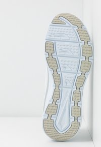 Semelle de chaussure de sport blanche avec sections de bande de roulement grises et grips à motifs, positionnée à la verticale contre un fond d’angle blanc.