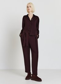 Completo bordeaux composto da camicia con collo e bottoni e pantaloni a gamba larga con cintura dello stesso tessuto, completato da stivaletti alla caviglia.